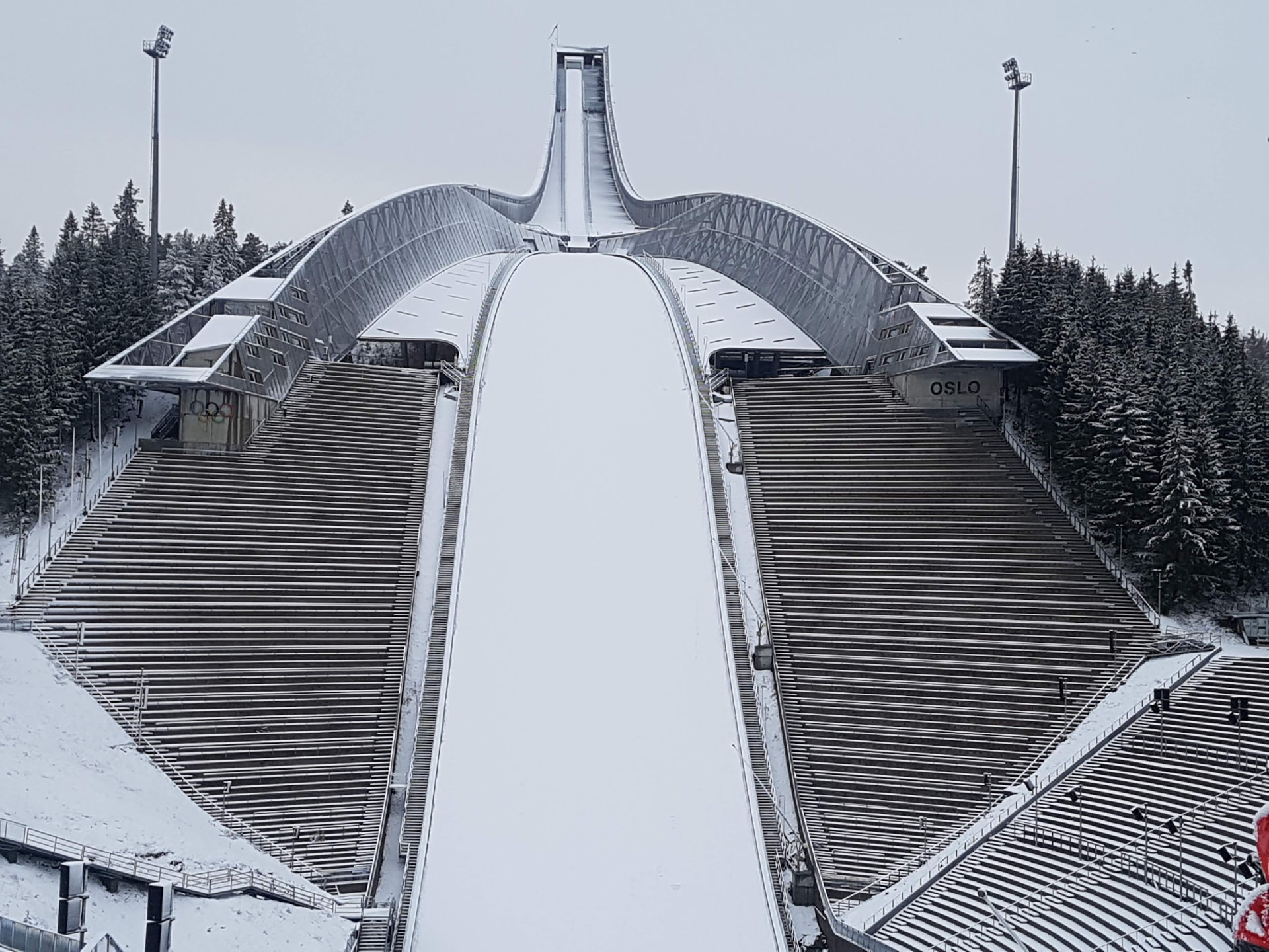 Holmenkollbakken sett forfra, med snødekt unnarenn, tomme tribuner og snødekte grantrær.